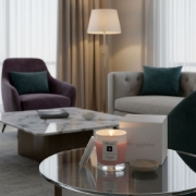 elenianna Milos Whispers of Love artisan candle creating a warm, sophisticated ambiance on a glass table in a modern living room.