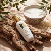 Cosmetic bottle on rustic wood with mastic resin tears, olive branches, and a bowl of donkey milk.
