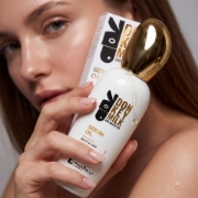 Close-up of a woman holding the Donkey Milk and Mastic Oil Serum Oil bottle with a drop of the lightweight dry oil visible on the gold cap.