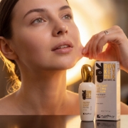 Close-up macro advertising portrait of a radiant young woman looking upwards, her hand gently pulling the skin of her neck to visualize the instant lifting effect. The 'mastic spa' Instant Lifting Serum bottle and box are prominent in the foreground with a golden light aura.