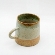 Handcrafted Mediterranean ceramic mug with moss green and speckled sand glaze on a white background.
