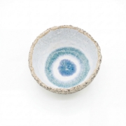 Top-down view of a handcrafted ceramic bowl with a speckled exterior and a blue concentric circle glaze inside.