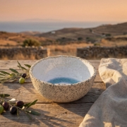 Artisan ceramic bowl on a rustic wooden table with fresh olives and branches during a Mediterranean sunset.