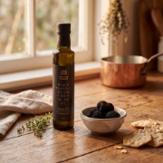 Lifestyle kitchen scene with Truffle Theory black truffle oil bottle, fresh truffles, and crackers on a rustic wooden table with warm natural light.