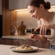 A young woman smiling while adding a finishing touch of black truffle olive oil and fresh truffle shavings to a steaming bowl of risotto.