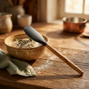 Rustic kitchen scene featuring a silicone spatula resting on a ceramic bowl with warm window lighting.