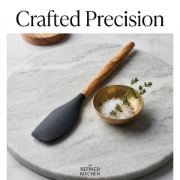 Editorial product photography of a black spatula on a marble platter with salt and fresh herbs.