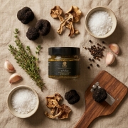 Overhead view of Truffle Theory Black Truffle Sauce jar with whole truffles, herbs, and garlic on linen