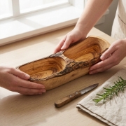 Hands holding a rustic Olea Wood Art olive wood appetizer plate on a kitchen counter