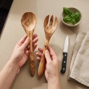 Hands holding a large Olea Wood Art personalized olive wood serving set over a beige kitchen counter