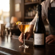 Milia Riza Blanc de Gris sparkling wine served in a Nick & Nora glass with a lemon twist on a dark bar counter